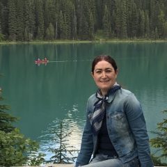 Firoozeh at a lake in the Rocky Mountains. A canoe paddles by behind her.