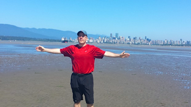John with his arms outspread with Vancouver behind him