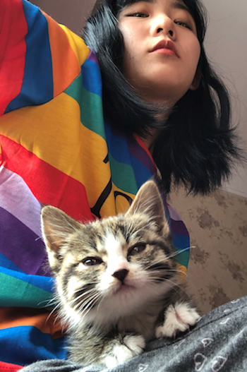 Shirely in a brightly coloured shirt with her cat in the foreground looking directly at the camera
