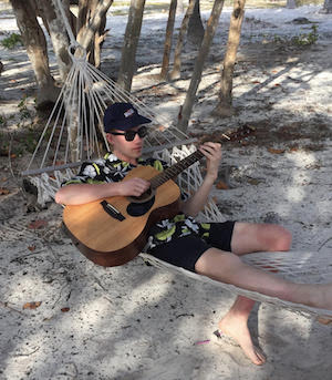 Camden wearing sunglasses lying in a hammock playing his guitar