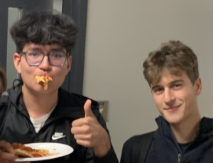 Two students, one has a face stuffed with pizza