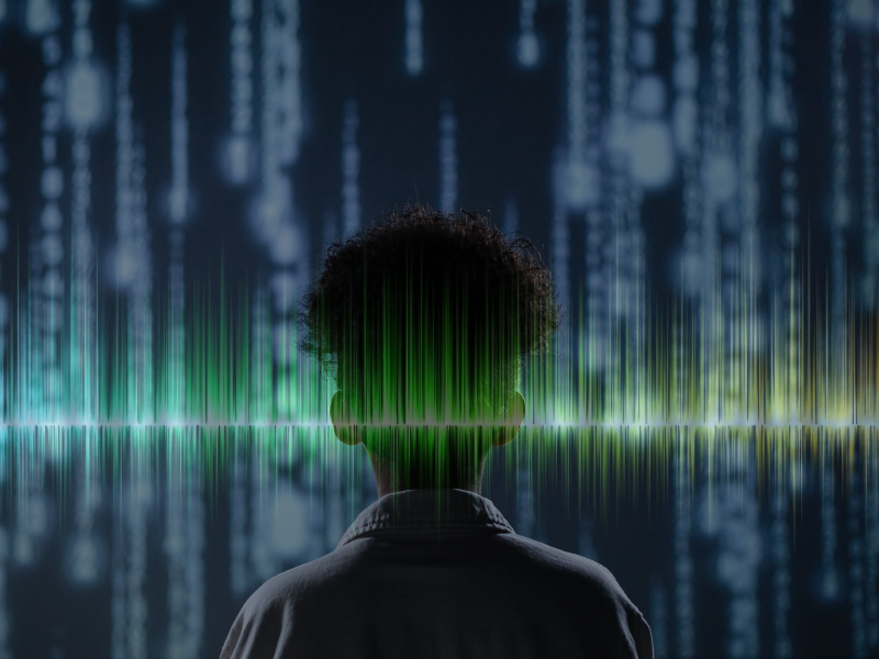 Person standing in front of lines of code, with sound wave spanning width of image