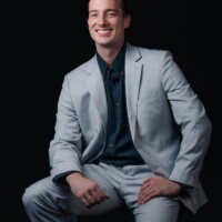 Dallas sitting comfortably in a suit with his hands on his knees