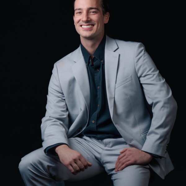 Dallas sitting comfortably in a suit with his hands on his knees