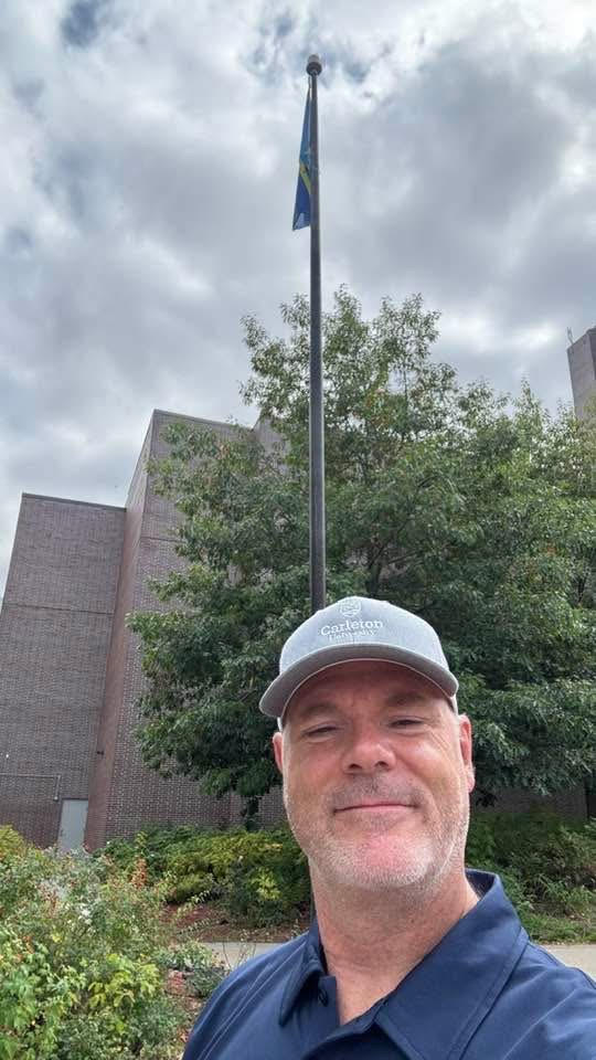 Image of David Morton in front of the WFD flag at Carleton University
