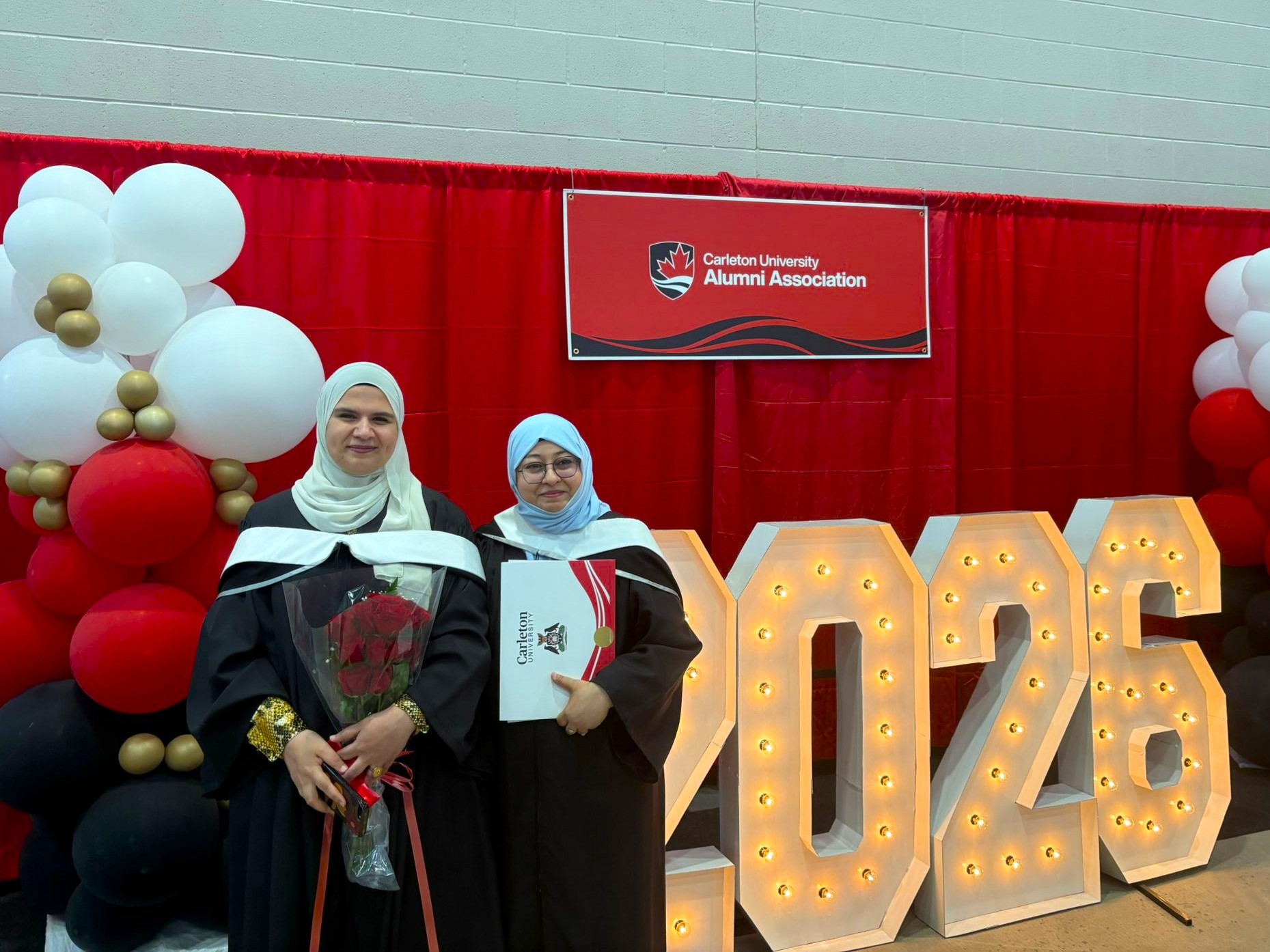 Graduates Asmaa and Mariam pose in front of 2026 sign