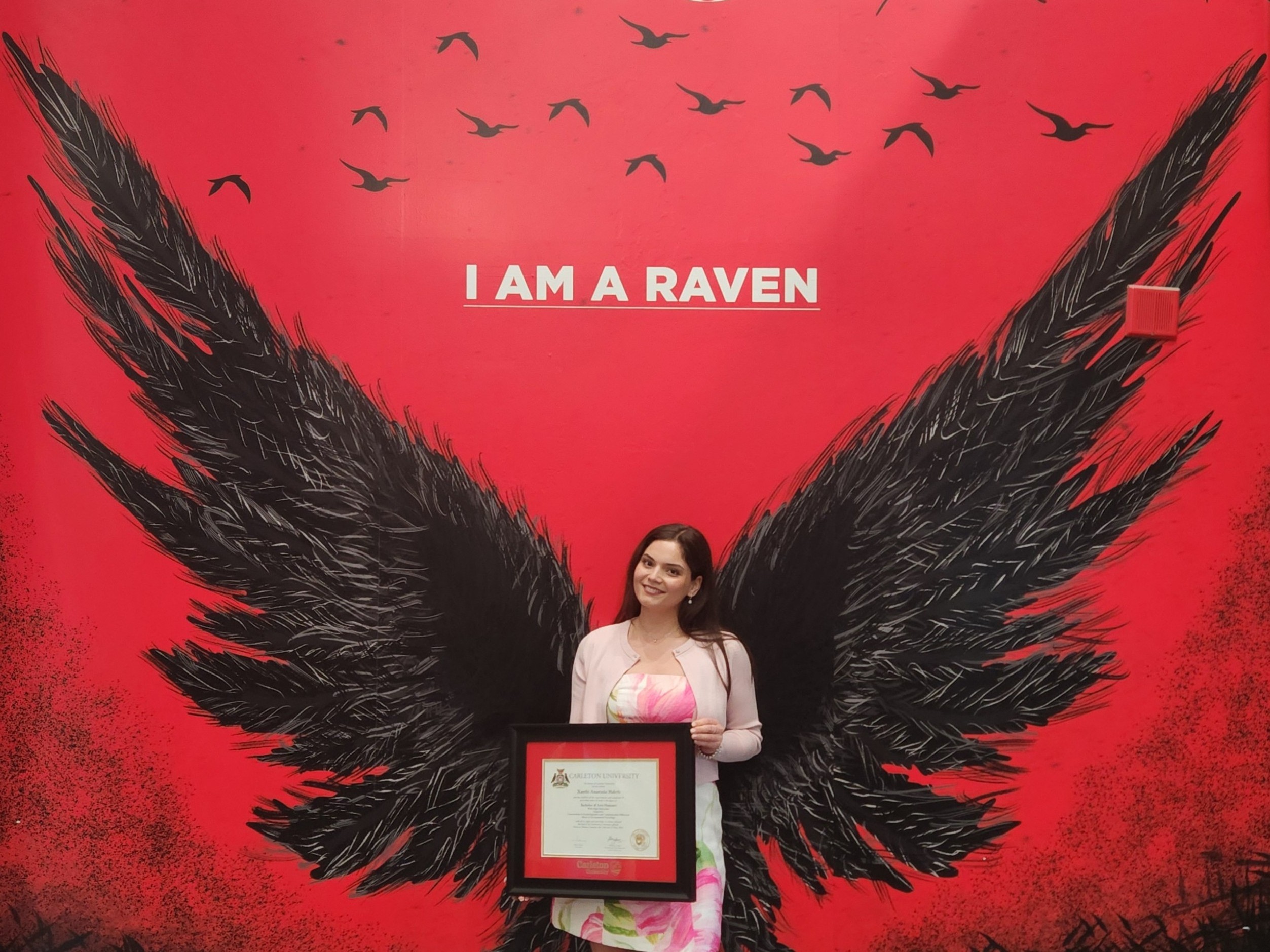 Image of a graduate, Xanthi, in front of a raven's mural