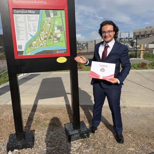 Thomas holding his degree in front of a map of the university