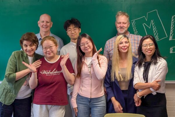 Group picture shows students and profs from TEAL program posing in front of a chalk board.