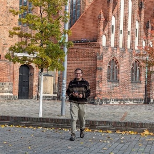 Thomas striding across the road in front of a gothic style church somewhere in Germany.