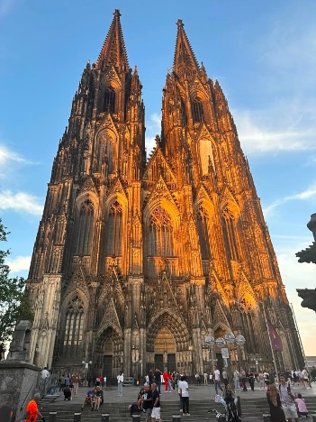Looking up at the top of Kölner Dom. Sunlight warming the stone. People on the steps in the foreground.