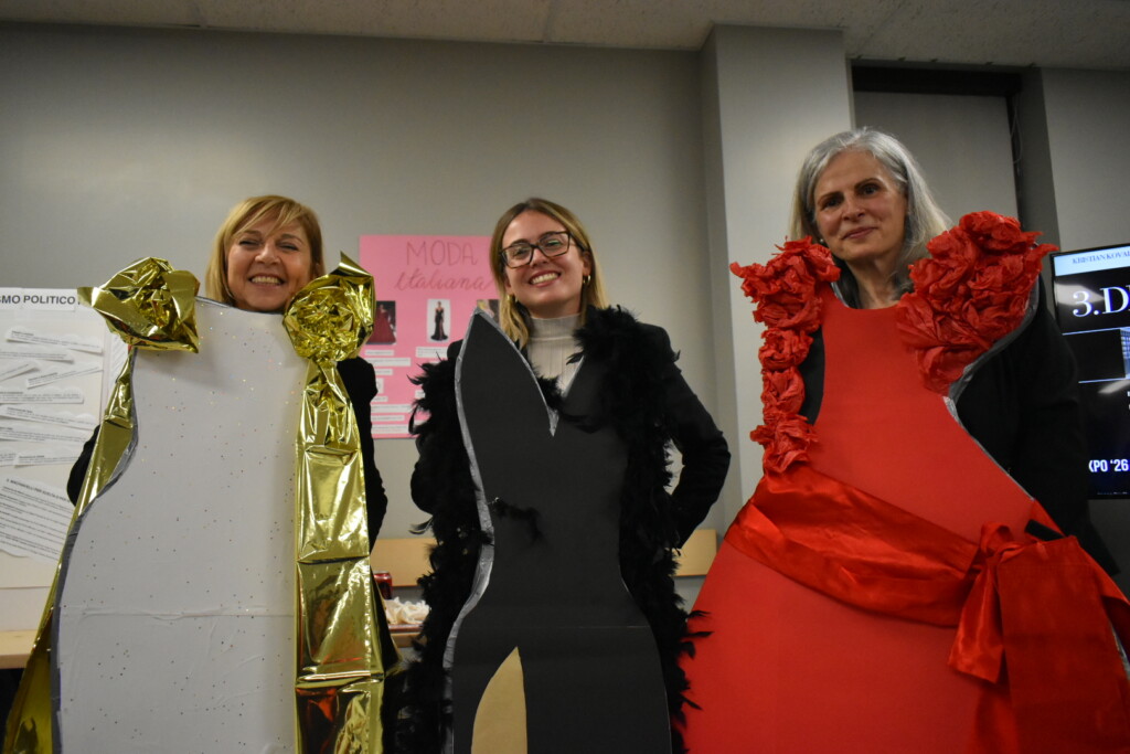 Marcella, Rebecca, and Claudia posing behind cutout models of dresses.