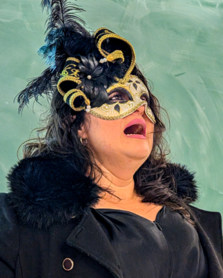 Shirley singing opera wearing black hat, boa, and mask