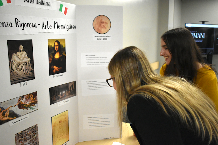 Rebecca leans in to examine Mirian's poster about Galileo and Davinci.