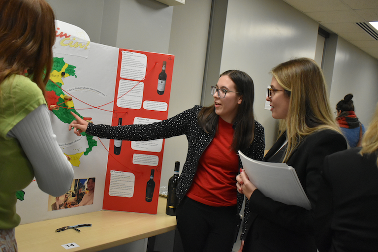 Chelsea points out wine regions on map of Italy. Rebecca looks on.
