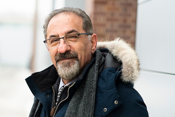 Jaffer Sheysholislami wearing glasses, a dark winter coat with a fur-trimmed hood, and a gray scarf.