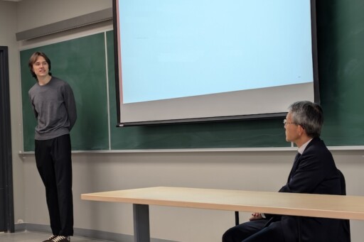 Lawrence standing at the front of the room as the Ambassador looks on.