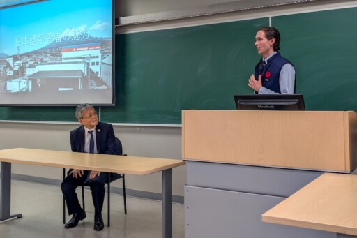 Marian standing at the podium while Ambassador listens with a slight grin on his face.