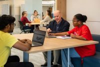 Don Myles with two students at a desk in the library