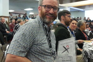 Mike seated poses with award
