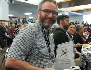 Mike seated poses with award
