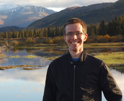 Christopher Cox in front of lake with a mountain in the background