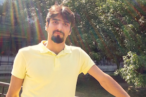 Hesam standing in front of some trees and leaning on a fence.