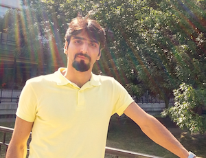 Hesam standing in front of some trees and leaning on a fence.