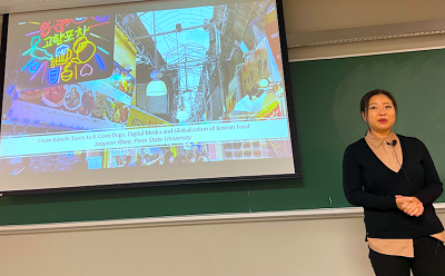 Dr. Rhee standing in front of her PPT. Slideshow shows a street scene in Osaka with many food signs.