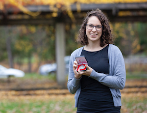 Mercedes displays her medal in front of an autumn landscape.