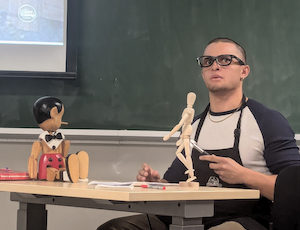 Gepetto in his workshop with Pinocchio puppet on the table and a wooden anatomical figure.
