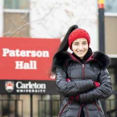 Talia smiling with arms crossed in front of Paterson Hall sign.