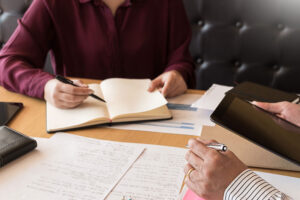 Teaching helping technology concept. Woman young teacher or tutor with adult students in classroom at desk with papers, laptop computer. Studies course.