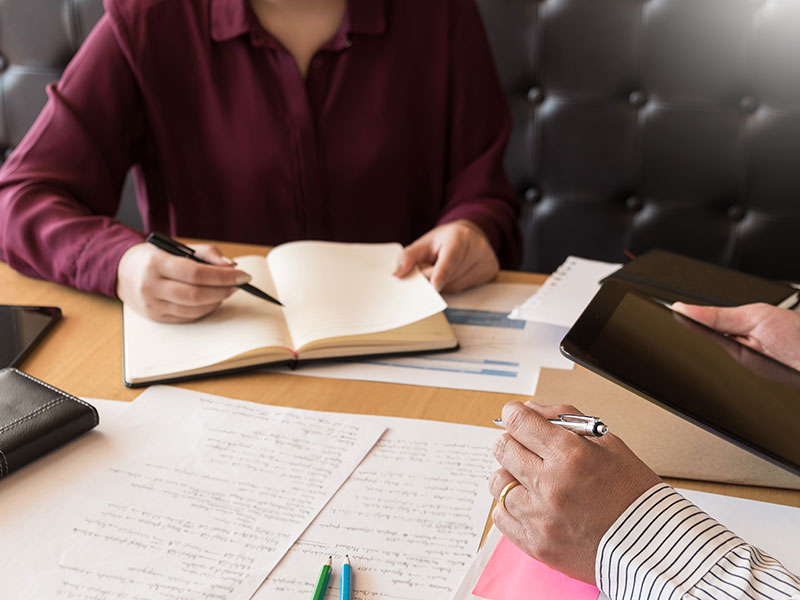 Teaching helping technology concept. Woman young teacher or tutor with adult students in classroom at desk with papers, laptop computer. Studies course.