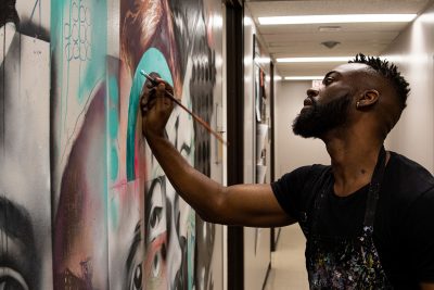 A photo of Allan Andre painting a wall mural in the entrance of the School of Social Work at Carleton University.