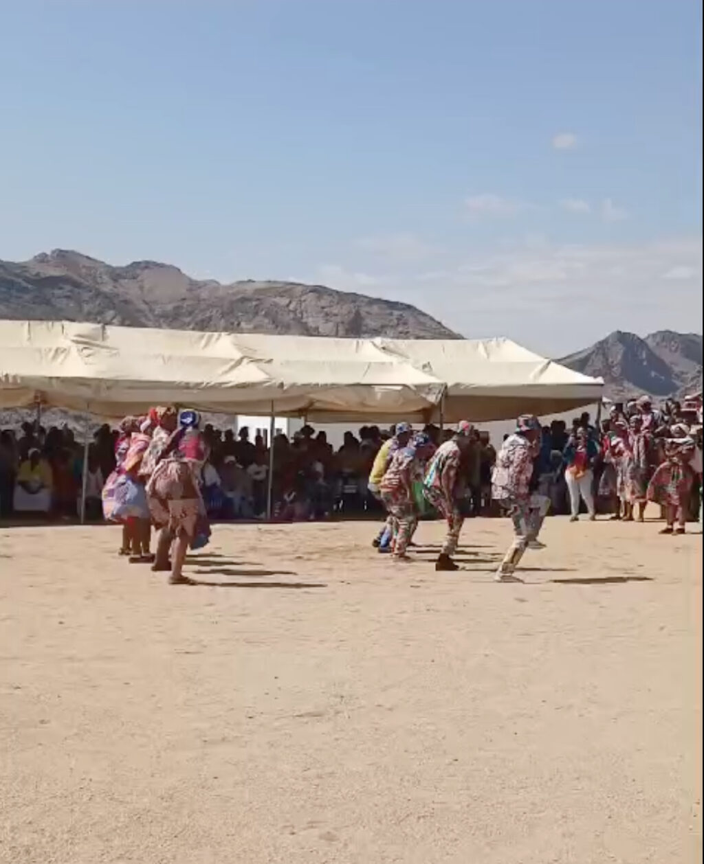 Image of an outdoor dance performance. There is a large crowd in the background of 100 or more people.