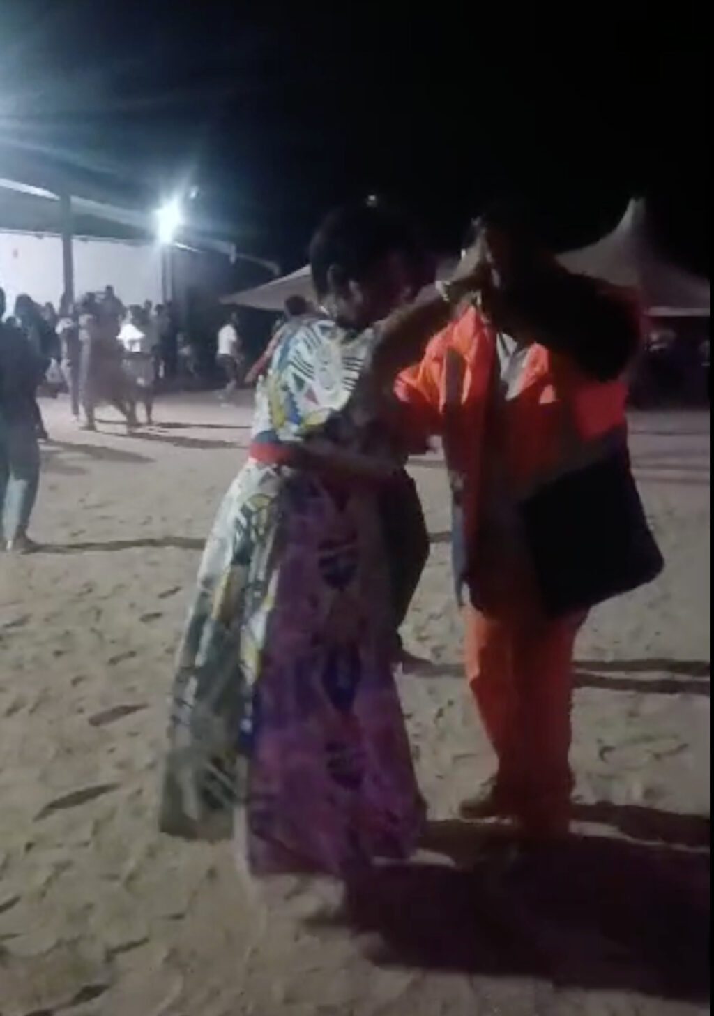 Image of a social dance outdoors at night, zoomed in on 2 performers in vibrant clothing.