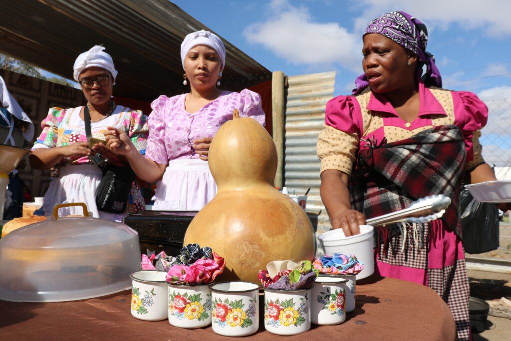 Vendors preparing a meal in front of a table dressing featuring Nama cups and a gourd.