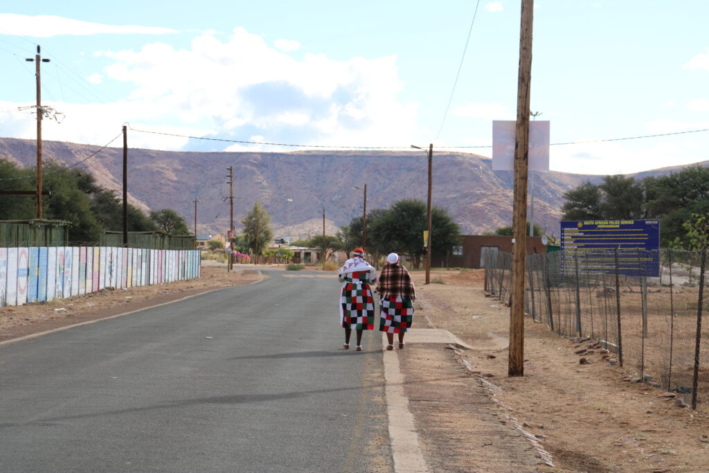 An image of two people walking on a road, with a large hill in the distance.