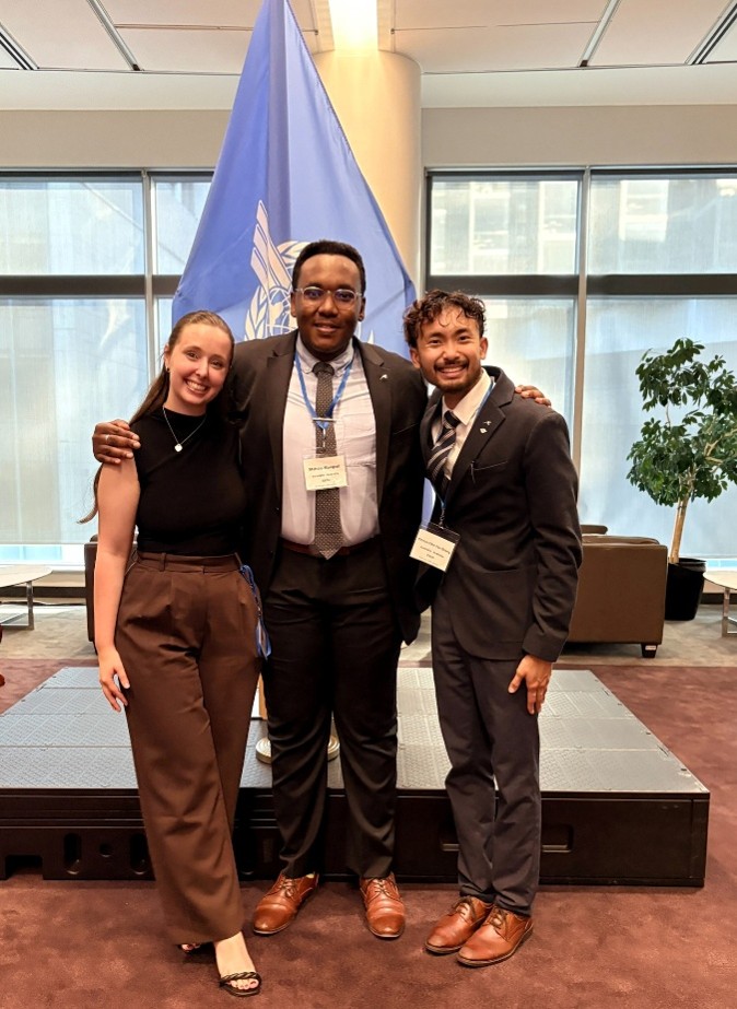 Three participants posing in front of ICAO flag