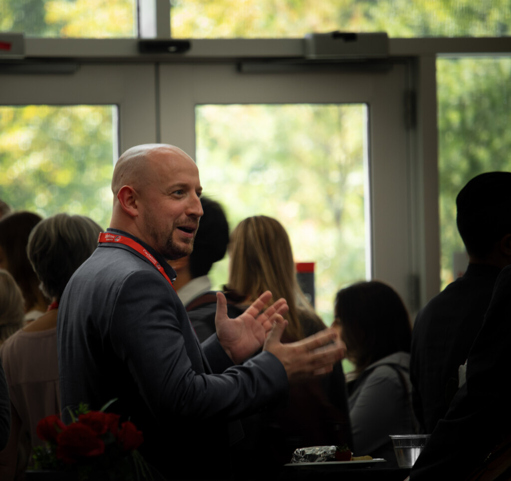 An attendee wearing a Carleton lanyard gestures while speaking with others during the Alumni Reception.