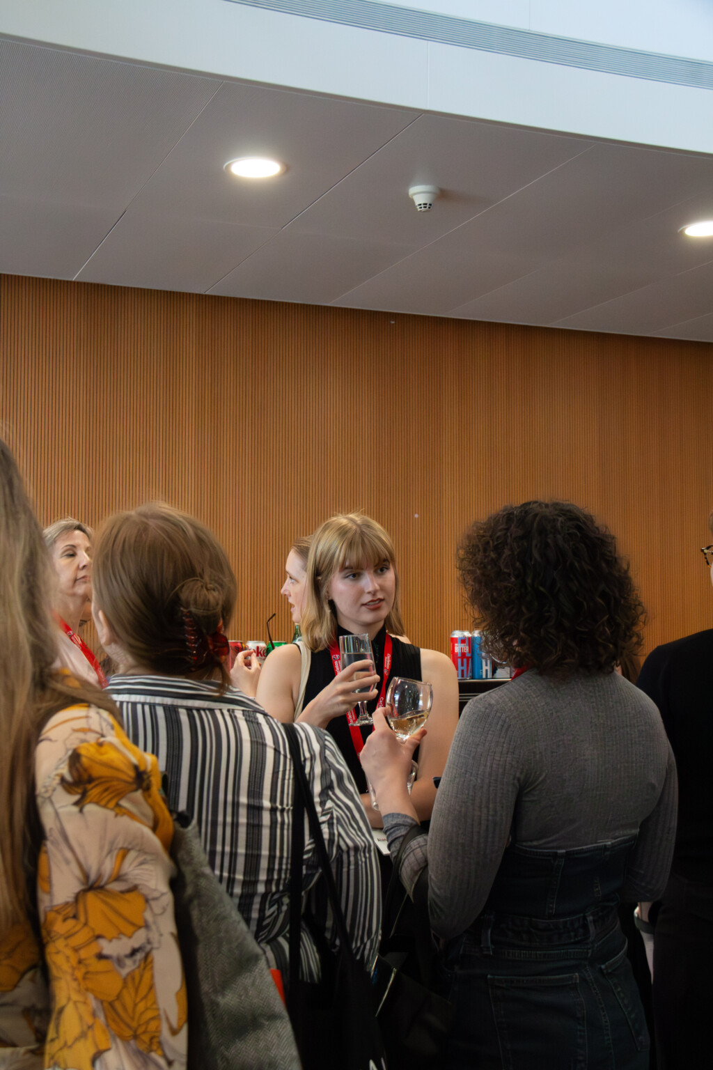 A group of attendees gather and talk in front of a wood-paneled wall.