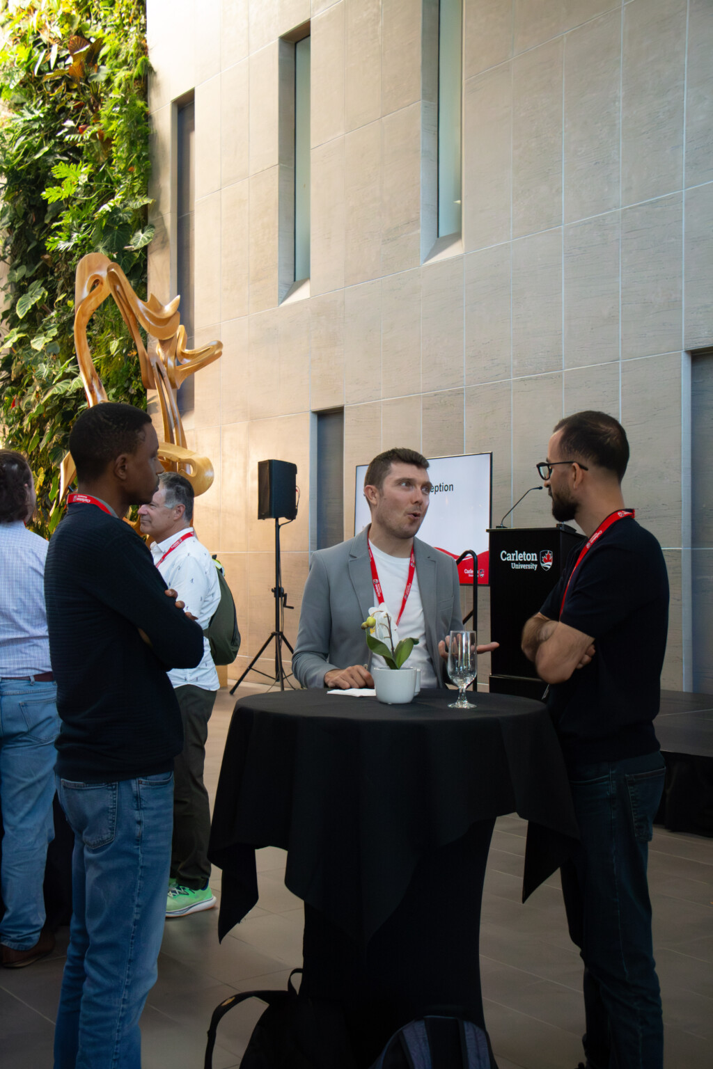 Attendees stand around a high-top table and converse during the Alumni Reception in Richcraft Hall Atrium.