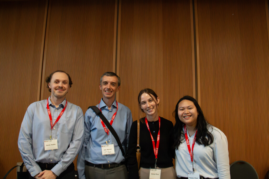 Attendees stand side by side in front of a wood-paneled wall.
