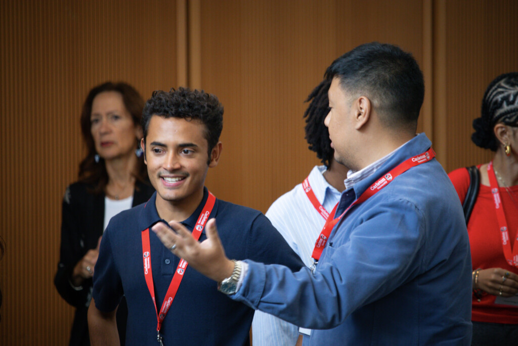 Attendees wearing Carleton lanyards chat during the Alumni Reception in front of a wood-paneled wall.