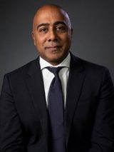 photo of arun, staring into camera wearing black suit and blue tie.