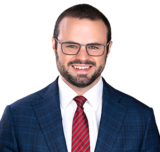 A photo of Trevor Neiman, with buzzed, dark brown hair and black glasses