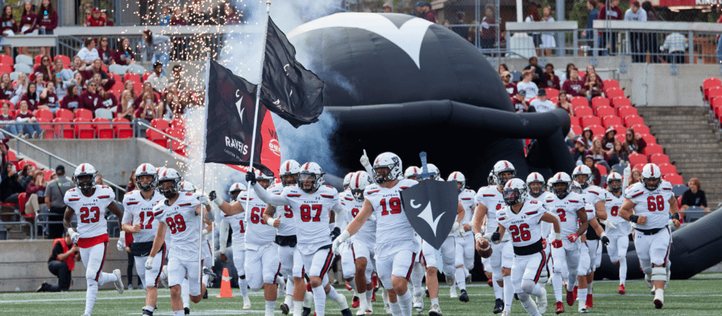 Ravens football players charge out onto the field at the Panda Game with flags, a shield, and other Ravens-themed props