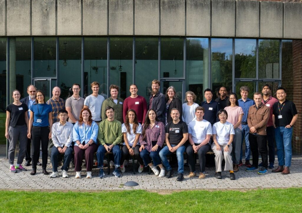 A Group Photo of approximately 30 people of Daniel Rosenbloom and research team. in front of grey building with windows