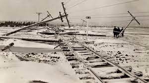 Non-colour photo of fallen telegraph poles on a railway line, with snow everyhwere